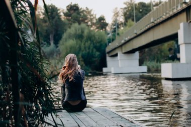 Güzel genç bir kadın kenarda oturmuş manzaraya bakıyor, iskelede dinleniyor.