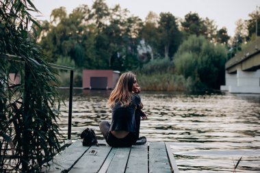Güzel genç bir kadın kenarda oturmuş manzaraya bakıyor, iskelede dinleniyor.