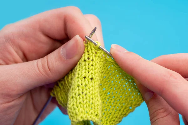 Close-up female hands knit on a knitting needle classic pattern of green threads on a blue background, copy space Royalty Free Stock Photos