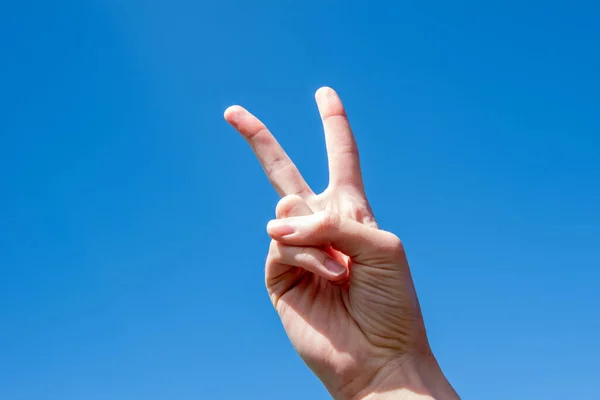 Symbol numer dwa w geście. Dwa palce białej kobiety pokazujące zwycięstwo lub gest pokoju na błękitnym niebie. — Zdjęcie stockowe