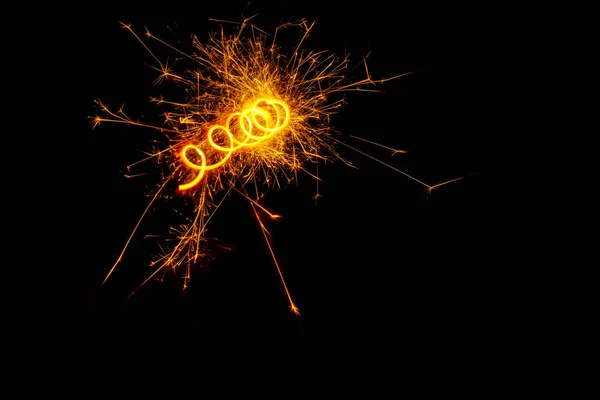 Uma espiral de luz de um sparkler ardente cintilante ou saudação em um fundo preto. Conceito de férias, espaço de cópia — Fotografia de Stock