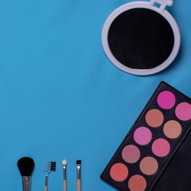 Renkli kozmetik fırçalar, göz farı, mavi arka planda ayna. Makyaj hazır. Düz konum, kopyalama alanı, tasarım için arkaplan