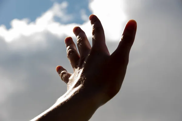 Empty open dark hand reaches for the clouds against the blue sky. Business concept, world concept, copy space.