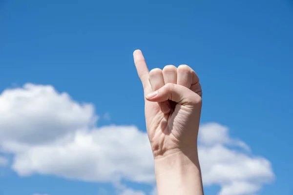 Hand clenched into a fist with an extended little finger on a blue background. Hand pointing little finger, concept of promising hand or reconciliation hand gesture in Asian countries