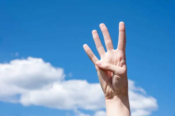 雲と青空の背景に隔離された4本の指を示す女性の手のジェスチャークローズアップ 手話記号番号4 — ストック写真