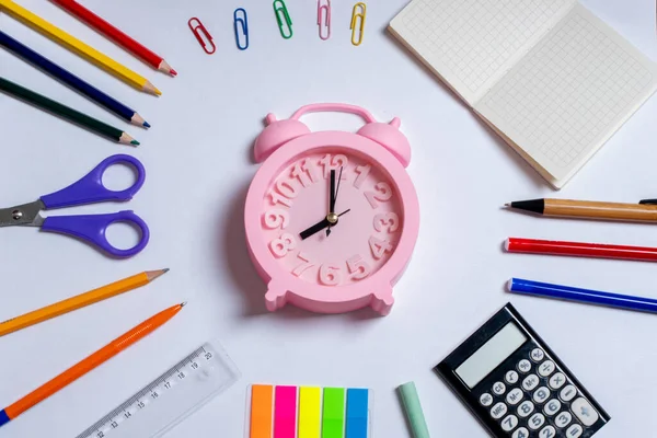 Yaratıcı düz görünüm okul konseptine dayanıyor. Renkli okul malzemeleri ve beyaz arka planda pembe alarm saati.