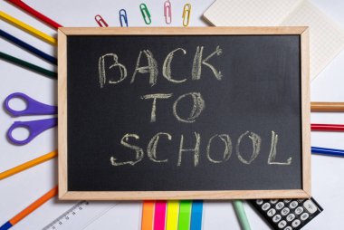 Yaratıcı düz görünüm okul konseptine dayanıyor. Renkli okul malzemeleri ve beyaz arka planda siyah karatahta.