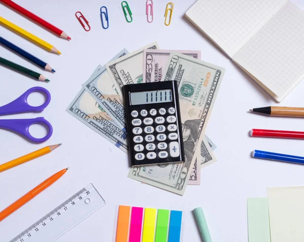 Вид сверху фотографии долларов и калькулятора в центре и цветных канцелярских принадлежностей, изолированных на белом фоне — стоковое фото