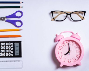 Okul konseptine, yaz zamanına ve eğitim konseptine karşı durmak için yaratıcı düz bir bakış açısı. Renkli okul gereçleri, gözlükler ve pembe alarm saati beyaz arka planda, kopya alanı, tasarım