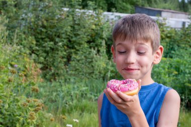 Çocuk lezzetli çöreğe şaşırdı. Parkta bir çocuk tatlı bir ziyafet veriyor. Sağlıksız gıda konsepti. Çocuklar tatlı yiyeceklere bayılır.