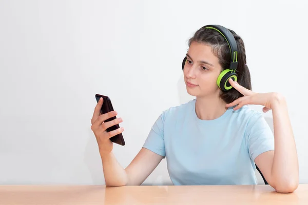 Retrato de una chica bonita adolescente escucha música en auriculares verdes y mira en un teléfono inteligente — Foto de Stock