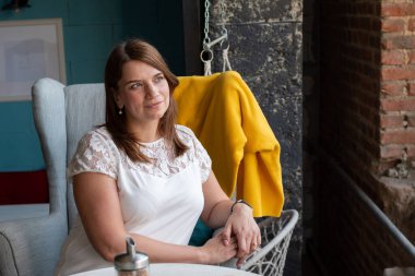 Beyaz bluzlu, kızıl uzun saçlı güzel bir kadın, kafede bir sandalyede tek başına oturmuş, emirlerini bekliyor..