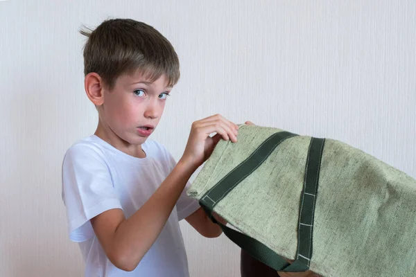 Portrait of a curious boy peeking behind an object hidden behind a green cloth. Concept of child curiosity, finding hidden objects by adults