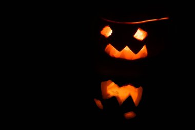 Jack Lantern siyah arka planda izole edildi. Siyah arka planda parlayan gözleri ve ürkütücü yansıması olan korkunç Cadılar Bayramı balkabağı manzarasını kapat.