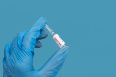Mavi eldivenli bir doktorun elinde mavi arka planda bir şişe COVID-19 ilacı ya da aşı bulunur. Koronavirüse karşı bir aşı geliştirildi. Boşluğu kopyala