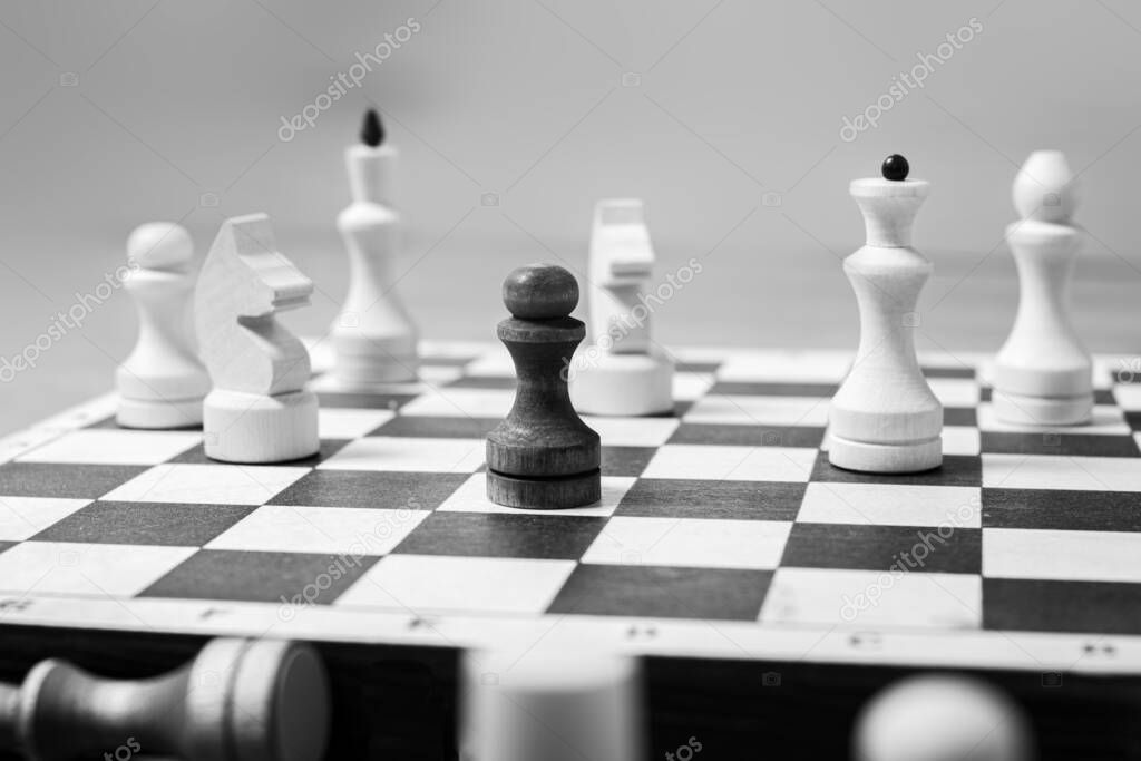One black pawn stands against a whole board of white chess pieces, selective focus, copy space. The concept is one against all. Leadership concept among competitors
