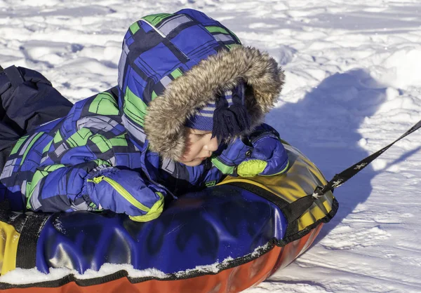 一个穿着冬衣的男孩在白雪上骑着一个充气雪橇 冬季户外运动概念 — 图库照片
