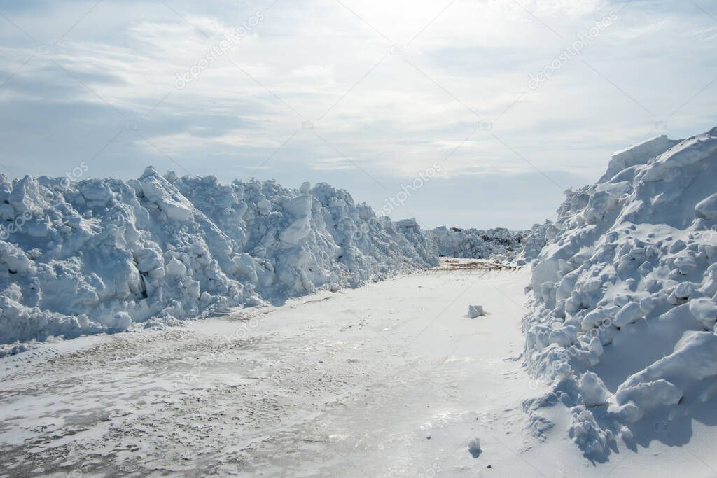 Large piles of snow on the side of the road for cars. High snowdrifts after a snowfall or blizzard. Can be used to illustrate road cleaning after snowfall