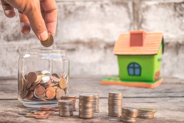 İleriki yatırımlar için para biriktirmek amacıyla cam şişeye bozuk para atın., Kredi, emlak merdiveni, finans, mortgage, emlak yatırımı, vergiler ve ikramiye kavramı.