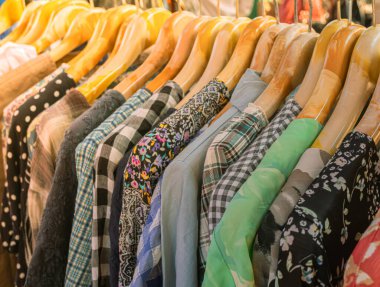Piyasadaki ahşap askılarda parlak renkli giysiler, açık hava pazarında kıyafet alışverişi, giysi ticareti..