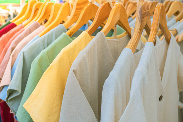 Яркие цвета одежды на деревянных вешалках на рынке, Магазин одежды на открытом рынке, Торговля одеждой.