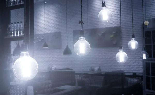 Many bulbs in the restaurant, The light of the lamp illuminates the restaurant, Dark background, Many electrical lamps bulbs hanging from ceiling at restaurant interior and glowing in darkness.