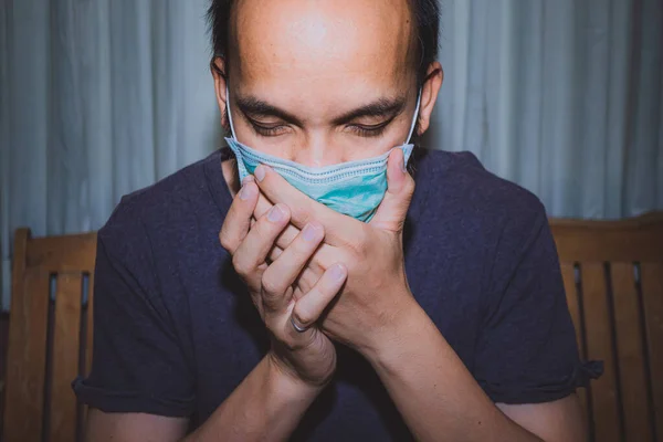 A sick man in a medical mask cough and holds his hands to his face, Man Wearing Face Mask feeling sick headache and cough because of Coronavirus Covid-19 in quarantine.