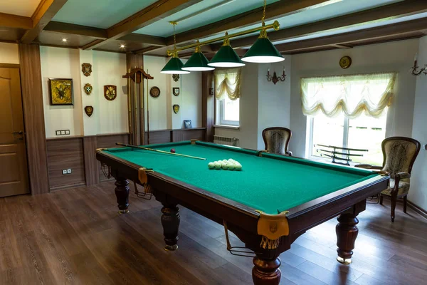 Billiard room interior. Green table for game. Old german style design. Brown wooden decor on the ceiling, walls and floor.