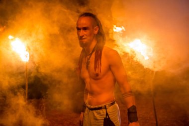 Irdorath grubu, sahne arkasında klip çekimi. Rastalı, kürk ve tekstil pantolon giyen beyaz adam. Viking 'in ormandaki gece vakti yanan meşalelerle aydınlanıyor.. 