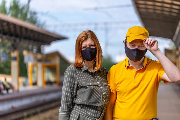 Safe family travel. Couple in face masks are waiting for train at the railway station. City view