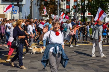MINSK, BELARUS - 30 Ağustos 2020: New Belarus, Minsk. Gri saçlı, beyaz kazaklı, kırmızı güllü kadın..