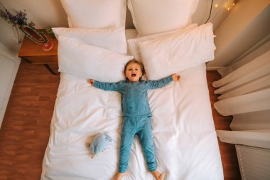 Küçük sarışın çocuk büyük bir yatakta zıplayarak ve oynayarak eğleniyor. Aile evde. Koronavirüs. Karantina.