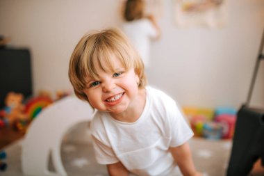 Sarışın çocuk evde kameraya bakıp gülüyor. Aile evde. Koronavirüs. Karantina.