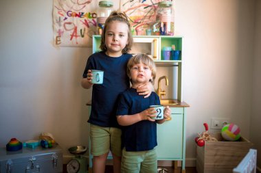 Küçük sarışın çocuklar karantina sırasında evde oyuncak bir mutfakla oynuyorlar. Evde eğlenmek. Aile eğlencesi