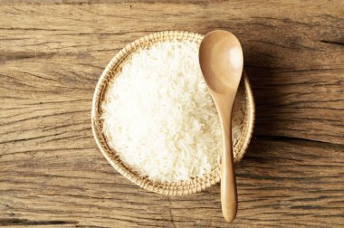 ahşap zemin üzerine kaşıkla hasır sepet içinde beyaz pirinç