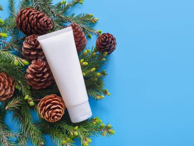 Doğal organik kozmetik ambalajlar, köknar konileri ve köknar dalları doymuş mavi arka planda. Boş beyaz tüp tasarımı yılbaşı dekoruyla birlikte. Kozmetik güzellik ürünleri markalaşma modeli.