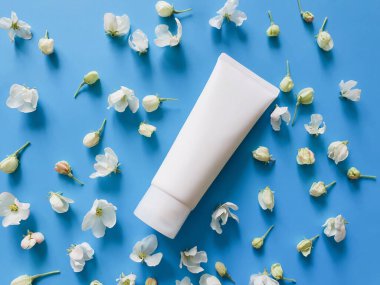Damgalamak için beyaz plastik tüp ve doymuş mavi arka planda küçük beyaz çiçekler. SPA kozmetik ürünü. Çiçek düzleştirildi ve taklit edildi. Üst görünüm