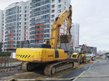 İki çeşit kazıcı. Bir yerleşim bölgesinde sarı inşaat ekipmanları. Yol onarımı.