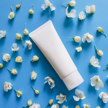 Krem, nemlendirici, losyon, yüz temizleyici ya da beyaz bahar çiçekleriyle dolu mavi bir arka planda şampuan. Moda gölge manzaralı kozmetik ürün için beyaz plastik kap. Düz yatıyordu.
