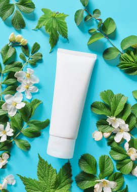 Markalaştırmak için beyaz plastik tüp ve doymuş turkuaz arka planda yeşillikleri olan küçük beyaz çiçekler. SPA kozmetik ürünü. Çiçek düzleştirildi ve taklit edildi. Üst görünüm