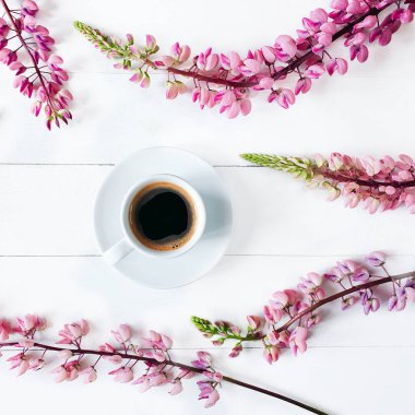 Beyaz bir fincanda sabah kahvesi ve yatay tahtalarda pembe lupinler beyaza boyanmış. Eski arkaplan, üst görünüm, düz yaşam biçimi.