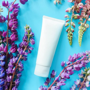 Güzellik spası tıbbi cilt bakımı ve kozmetik losyon şişesi krem ambalaj ürünleri mavi arka planda çok renkli çiçeklerle birlikte. Genel bakış. Çiçekli düz yatak, yaşam tarzı. Temiz güzellik kavramı