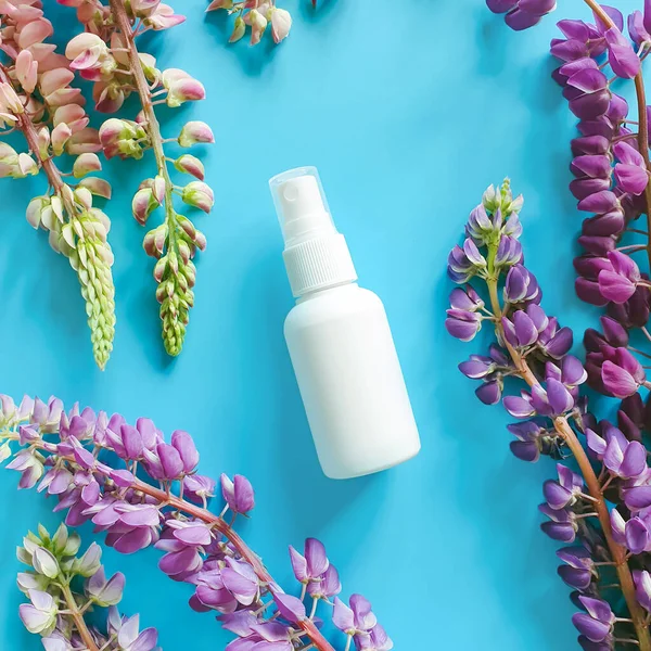 Top view and close-up of white plastic spray bottle mock-up and flower lupine composition on a blue background. Natural organic spa cosmetics and liquid antimicrobial spray concept. Flat lay stylish.