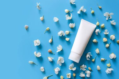 İlaç ya da kozmetik ürünleri markalaştırmak için kullanılan beyaz sıkılmış plastik tüp modelinin üst görüntüsü - krem, jöle, cilt bakımı, diş macunu. Mavi arka planda çiçek açan kiraz çiçekleri. Spa kozmetik ürünü