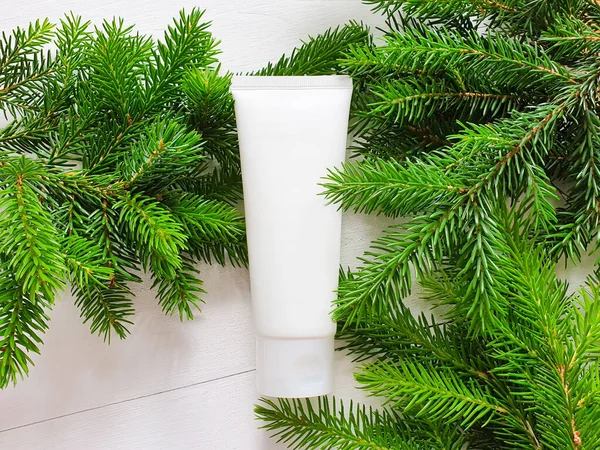 Beyaz sıkılmış plastik tüpün 3D modelinin üst görüntüsü. Ahşap arka plan ve bir Noel ağacının dalları. Doğal organik kozmetik kavramı. Noel hediyesi konsepti.