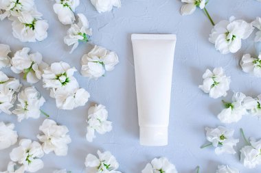 Beyaz sıkılmış plastik tüpün model modelinin üst görüntüsü. Pastel gri arka planda küçük beyaz çiçekler. Doğal organik kozmetik konsepti.
