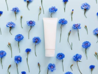 İlaç ya da kozmetik ürünleri markalaştırmak için kullanılan beyaz sıkılmış plastik tüplerin üst görüntüsü. Krem, jöle, cilt bakımı. Kozmetik şişe kabı üzerinde ve mavi çiçekli pastel mavi arka plan.