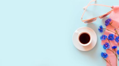 Mavi çiçekli bir fincan kahve, pembe güneş gözlüğü ve pastel mavi arka planda pembe ipek kurdele. Yaz plajı yatıyordu. Yaşam biçimi, kopyalama alanı, modelleme.