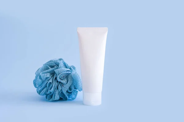 Mock-up of white squeeze bottle plastic tube for branding of medicine or cosmetics - cream, gel, skincare, toothpaste. Cosmetic bottle container and sponge on blue background. Minimalism