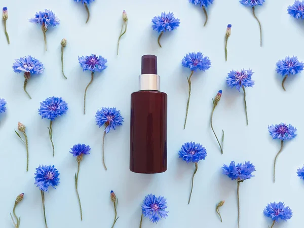 Mock-up of unbranded brown plastic spray bottle and blue cornflowers on a pastel blue background. Cosmetic bottle container for branding of medicine or cosmetics. Natural organic spa Body mist.